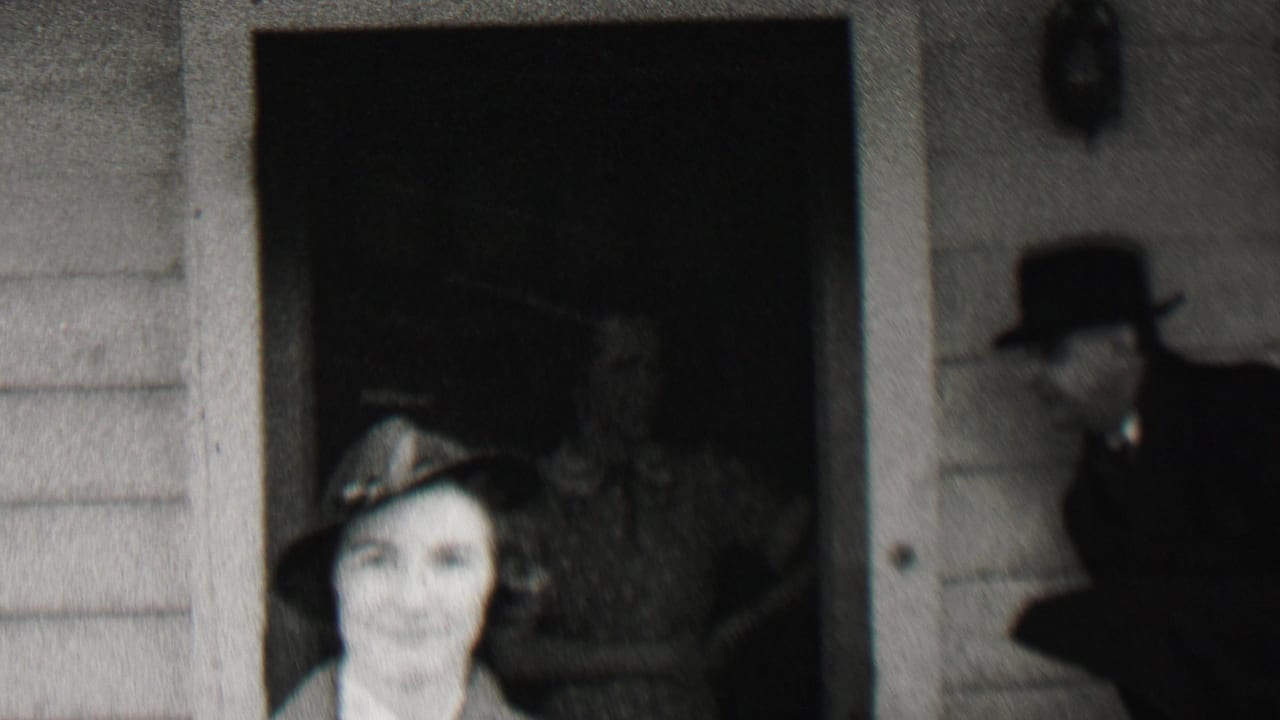 A woman in a small hat faces the camera outside the Beachwood house, with dark doorways, clapboard siding, and partially visible adults in hats around her.