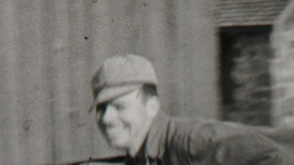 In 1937 Beachwood, New Jersey home-movie footage, a blurred man in a cap passes close to camera while two adult men stand smiling outside a clapboard house.