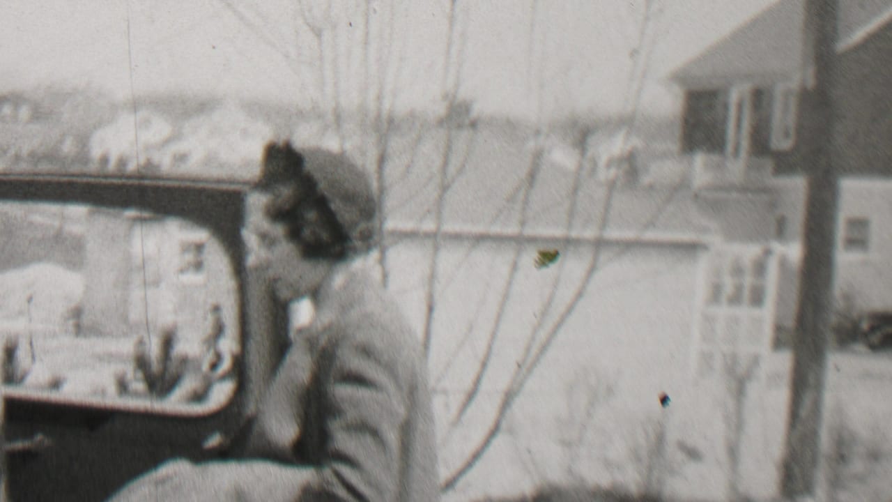 Woman turns toward an open car door with houses and bare trees in the background.
