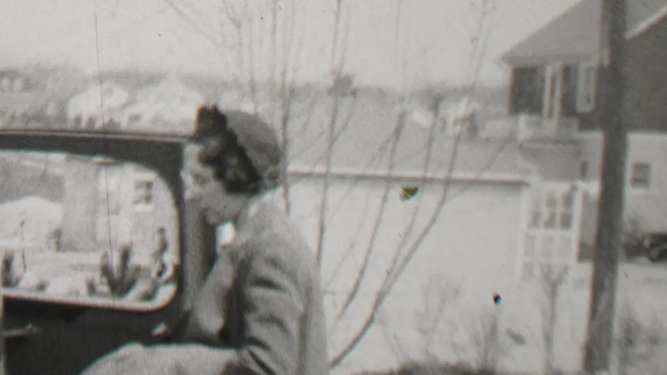 The woman is seen in profile near an open automobile door, with the car window framing part of the residential street behind her in Beachwood, New Jersey.