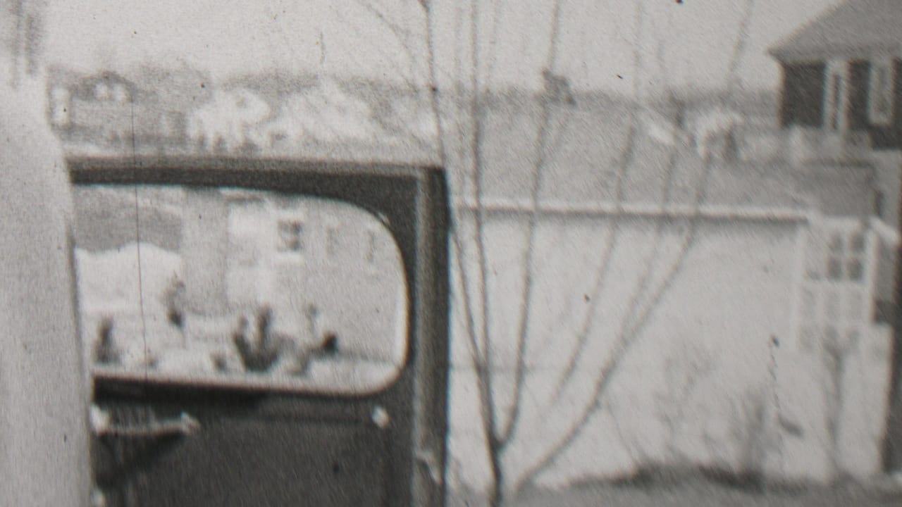 Beachwood, New Jersey home-movie frame from 1937 showing a soft, grainy view of a vehicle or vehicle body beside a residential building with bare tree branches in front.