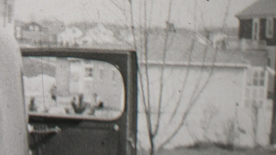 Beachwood, New Jersey home-movie frame from 1937 showing a soft, grainy view of a vehicle or vehicle body beside a residential building with bare tree branches in front.