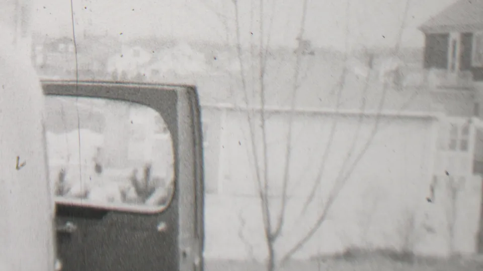 Beachwood, New Jersey home-movie frame from 1937 with a pale residential building, leafless trees, and a partially visible vehicle or vehicle body along the left edge.