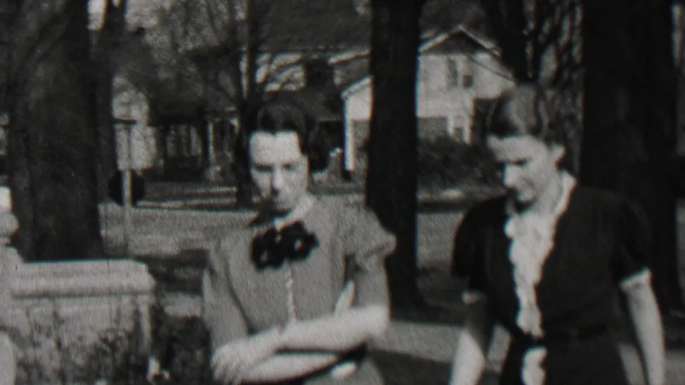 Beachwood, New Jersey 1937 home-movie frame showing two adult women in period dresses walking side by side through a residential neighborhood with houses and bare trees behind them.
