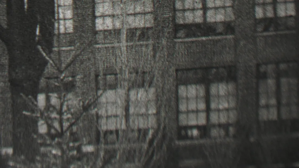 1937 Beachwood, New Jersey 8mm frame showing a wider facade view with repeated windows, brick or stone walls, and leafless branches crossing the foreground.