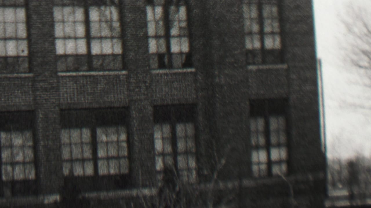Black-and-white 1937 Beachwood, New Jersey home-movie frame showing a large brick residence or institutional-looking house at left and neighboring homes with parked cars at right.