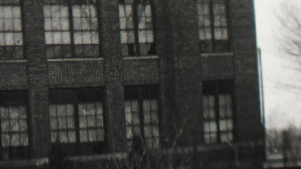 Black-and-white 1937 Beachwood, New Jersey home-movie frame showing a large brick residence or institutional-looking house at left and neighboring homes with parked cars at right.