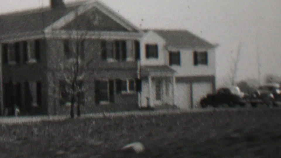 Black-and-white 8mm frame from Beachwood, New Jersey in 1937 showing a substantial two-story house with a columned porch, shuttered windows, bare trees, and cars along the street.