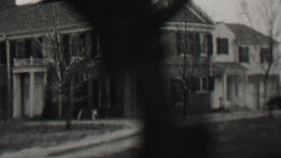 1937 black-and-white home-movie frame showing residential houses in Beachwood, New Jersey, with porches, lawns, bare trees, and a dark vertical artifact from the moving 8mm image.