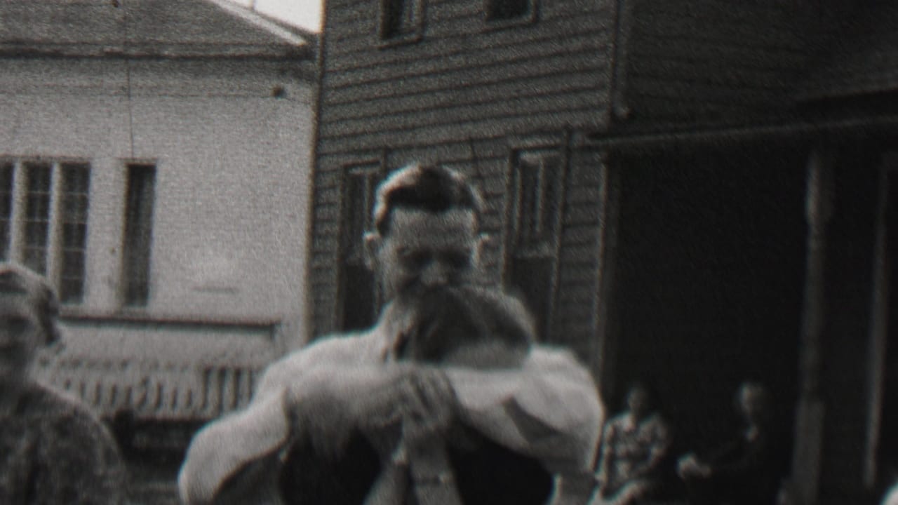 In 1937 Beachwood, New Jersey home-movie footage, a man in a light shirt and suspenders holds a woman close on a porch in front of a clapboard house.