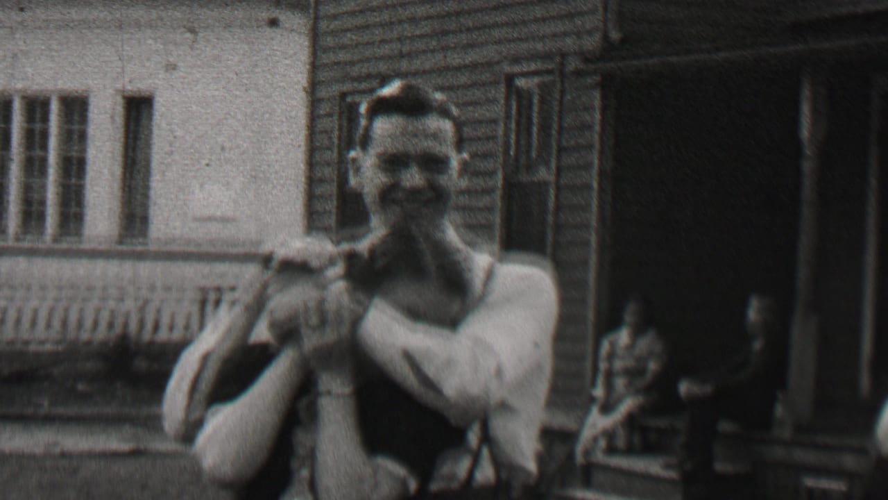Smiling man holds a woman close in front of a house porch and open doorway.