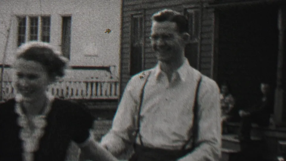 The couple separates slightly and smiles toward the camera, showing the woman's dark dress with light collar and the man's light shirt and suspenders.
