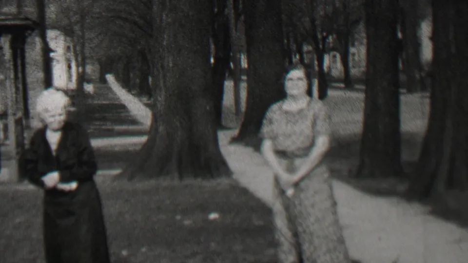 Two women in period dresses stand near a tree-lined sidewalk and porch steps in the supplied Beachwood, New Jersey 1937 home-movie scene.