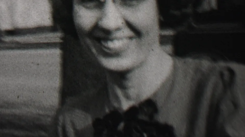 A smiling woman appears close to the camera in a 1937 Beachwood, New Jersey 8mm home-movie frame, with a tree and residential background partly visible.