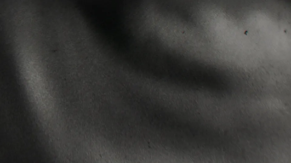 A very soft black-and-white 8mm frame shows part of a person's face and shoulder near the lens, with little background detail visible.