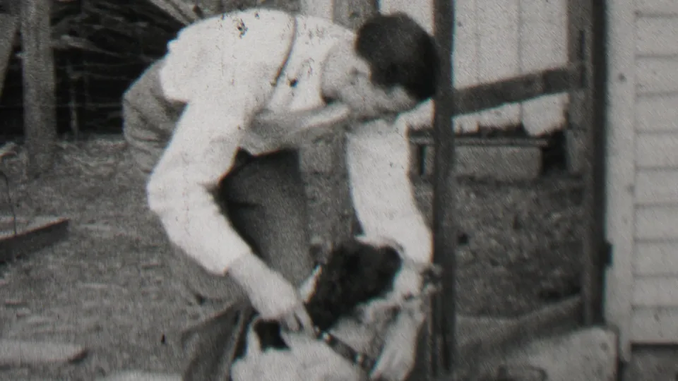 The man crouches close to the small black-and-white dog near a porch post and wood-sided structure in the Beachwood, New Jersey backyard scene.