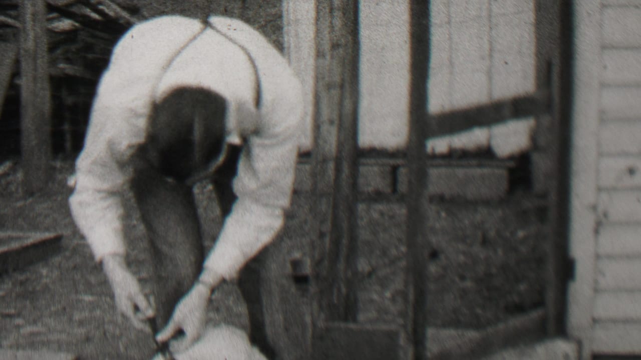Man leans over with his hands near a small dog by wooden siding.