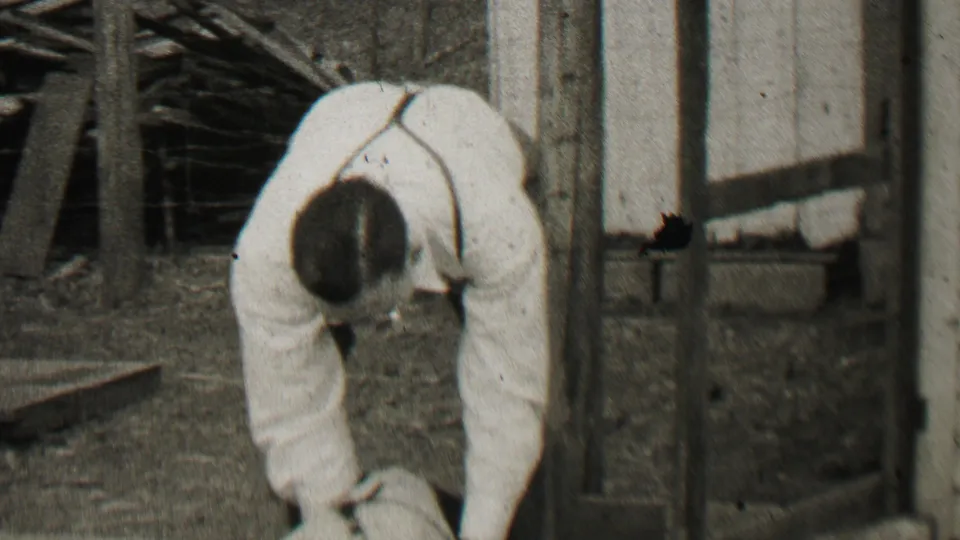 The 8mm frame shows the man bending lower over the dog, with the animal partly cropped at the bottom and the wooden structure still visible behind him.