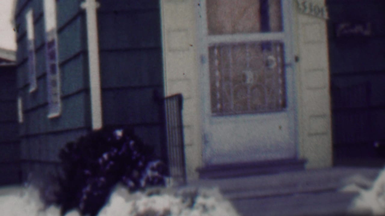 Closer view of the front door area, porch railings, dark siding, snow, and shrubbery.