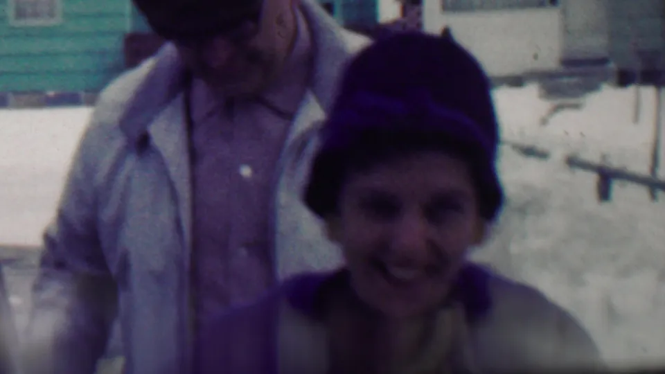 In this 1958 Grand Rapids home-movie frame, two bundled adults appear near a house in a snowy residential setting, with the foreground face soft and partly shadowed.
