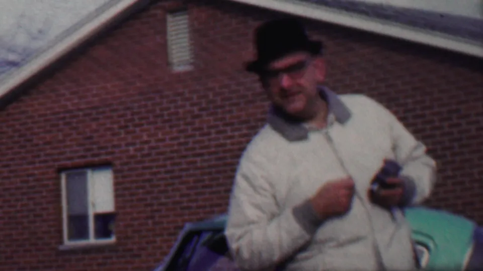 The man remains near the green car, holding a small object and facing the camera against the red brick building visible in the supplied Grand Rapids metadata.