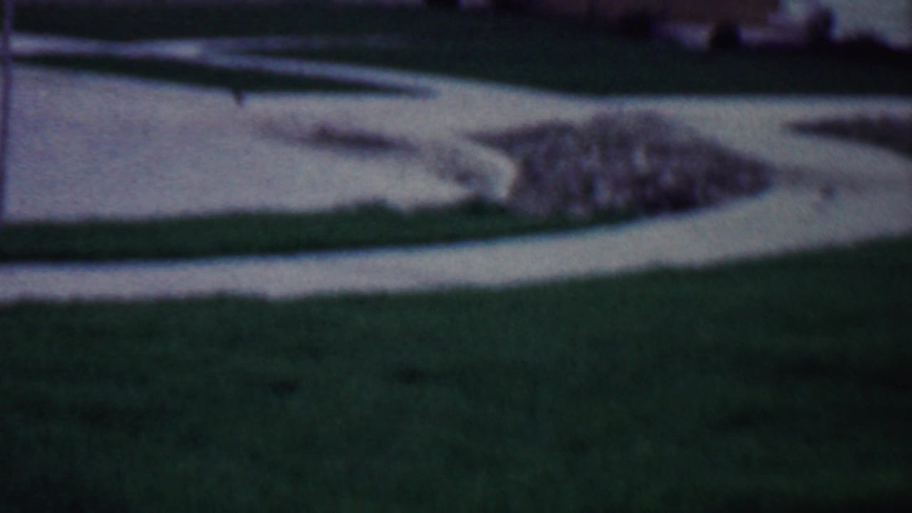 Lawn and curved concrete path with a rubble pile near a house.