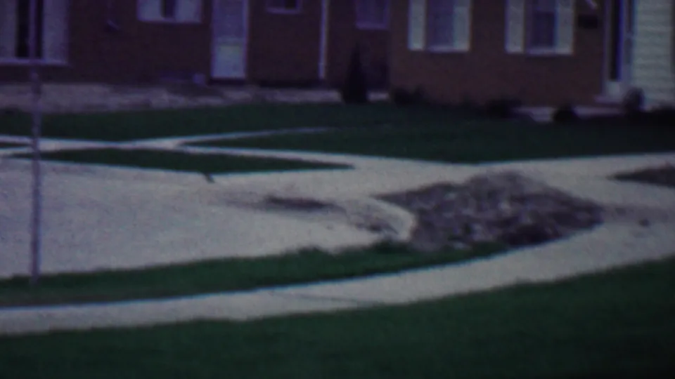 Late-1950s Grand Rapids residential view showing a winding concrete path through a lawn, a small rubble pile, a slender yard post, and brick houses beyond.