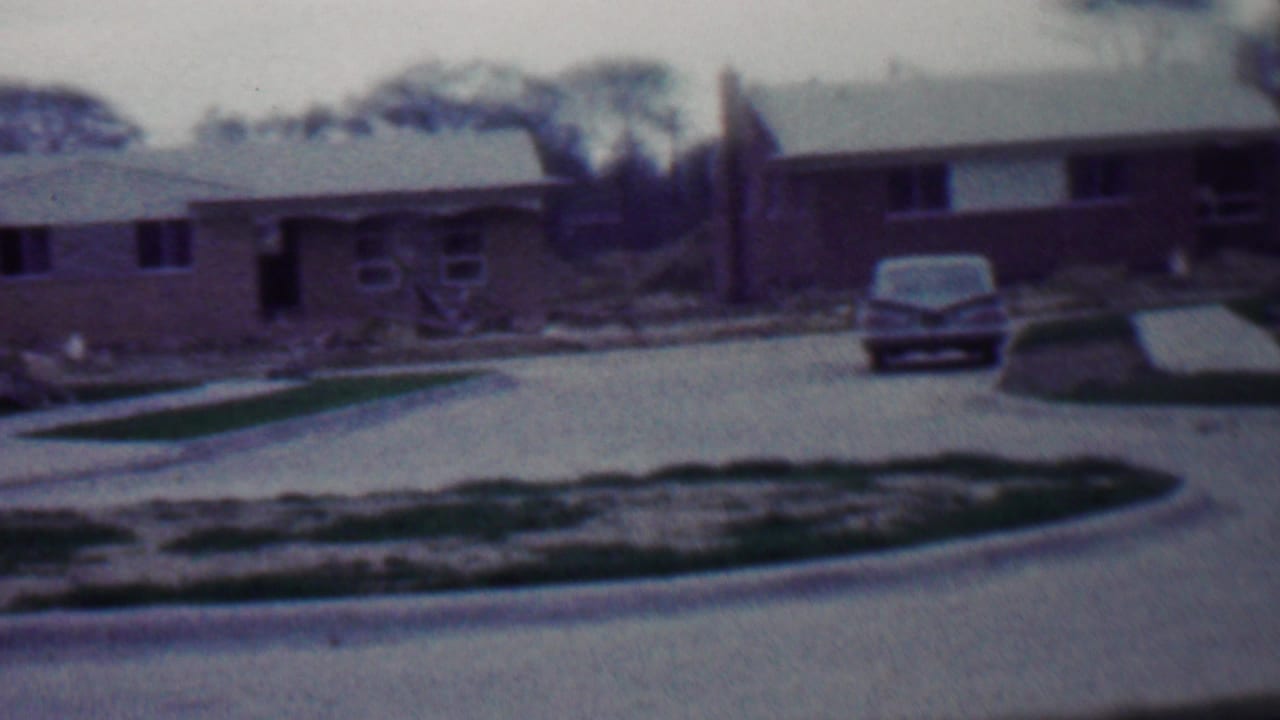 1958 Grand Rapids neighborhood view showing brick ranch-style houses, a parked mid-century car, fresh pavement, and unfinished landscaping.