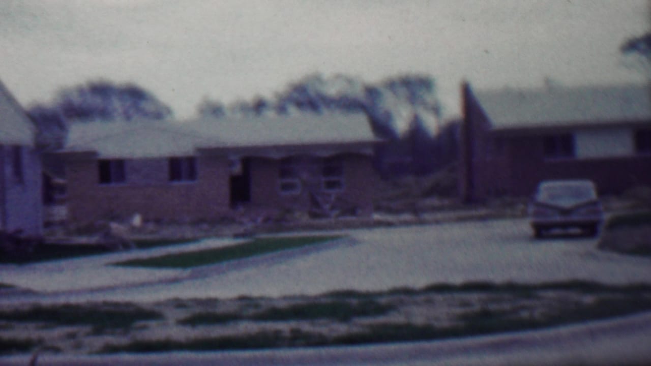 Grand Rapids residential street in 1958 with a brick house, fresh driveway, parked car, sparse grass, and signs of recent construction.