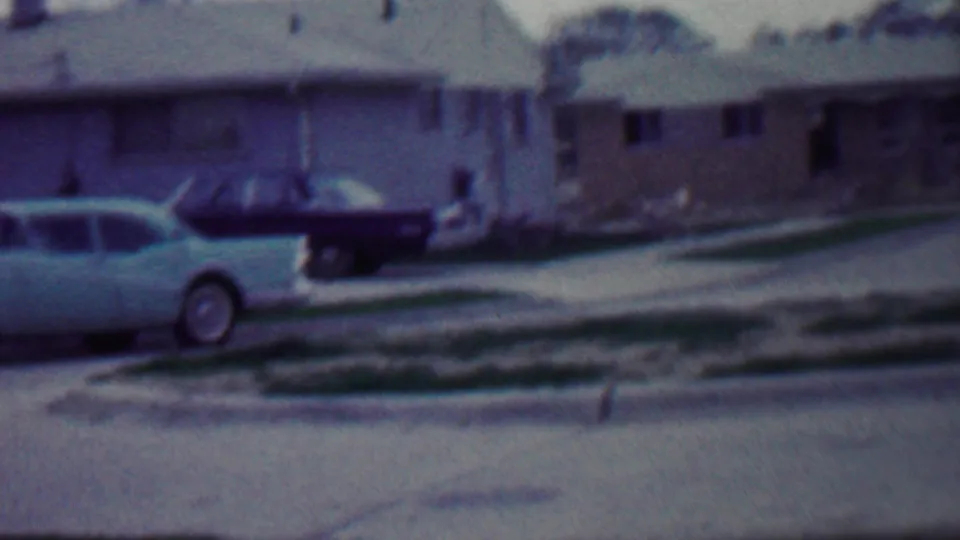 Grand Rapids suburban street in 1958 with a light-colored station wagon, brick and light-sided houses, driveways, and unfinished lawns.