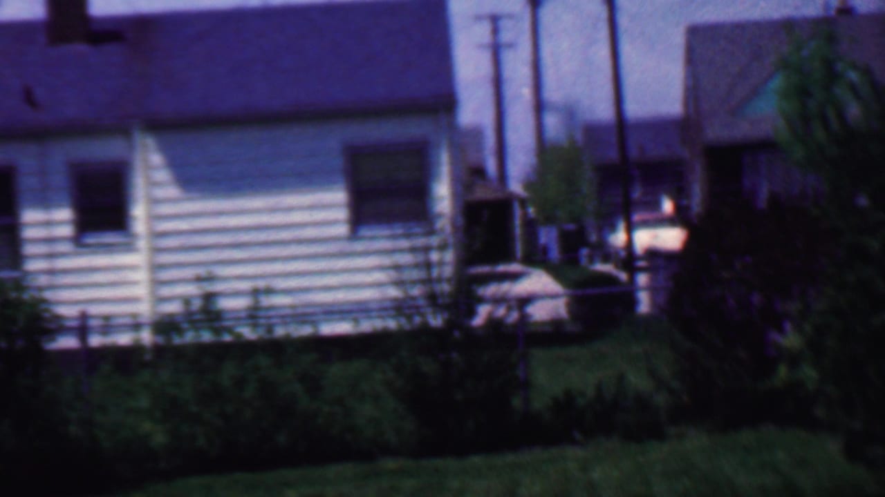 House exterior with horizontal siding, window, shrubs, lawn, utility poles, and parked car.