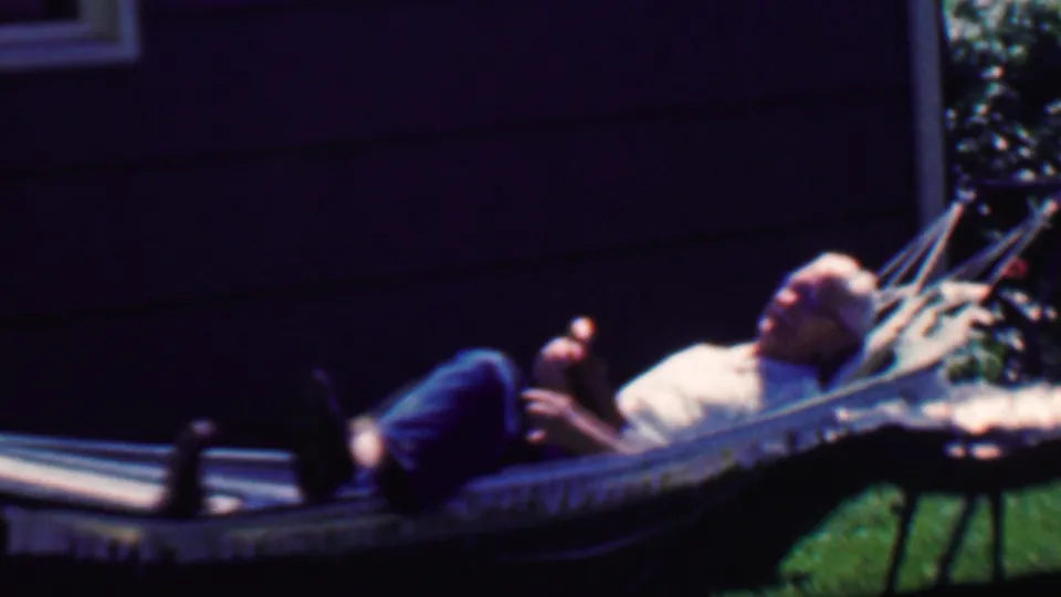 A 1958 Grand Rapids backyard frame shows the man relaxing in the hammock with his legs up, one hand raised, and a house window partly visible behind him.