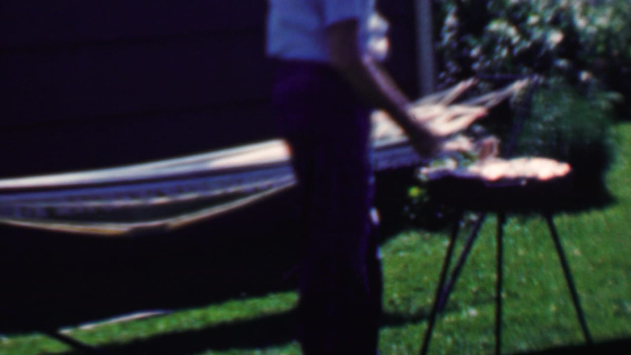 Standing man near a hammock and small round grill in a sunny backyard.