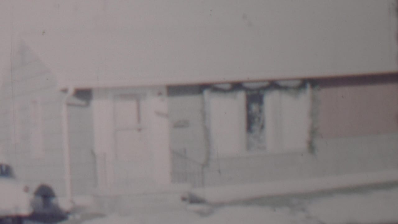 A similar 8mm view of the Lincoln, Nebraska house exterior, showing snow along the front walk, the doorway, and a dark-curtained window under a pale winter sky.