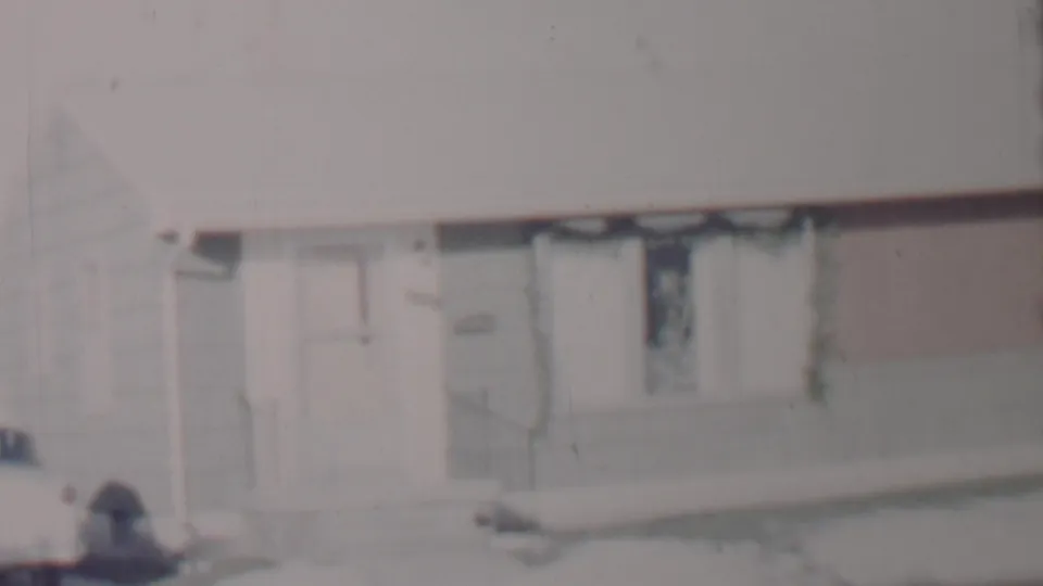 A similar 8mm view of the Lincoln, Nebraska house exterior, showing snow along the front walk, the doorway, and a dark-curtained window under a pale winter sky.