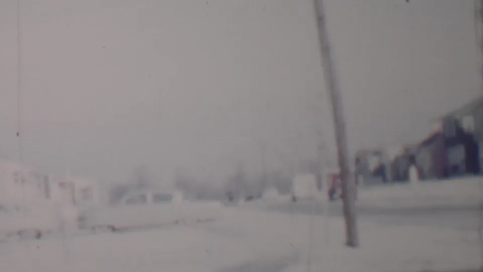 Wider Lincoln, Nebraska residential street view from the 1962 metadata, showing snow along the road, distant houses and vehicles, a utility pole, and indistinct roadside detail.