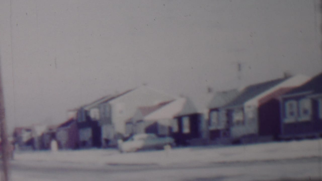 Row of snow-covered houses with parked cars along a quiet residential street.