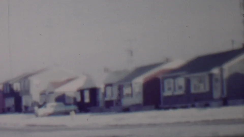 Blurred handheld 8mm frame showing snow-covered rooftops, modest suburban houses, and a parked car on a Lincoln, Nebraska residential street.