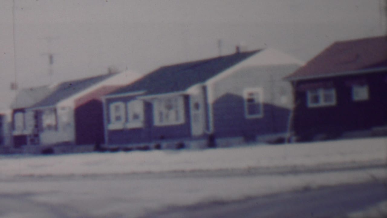 A 1962 8mm home-movie frame shows a snow-covered suburban street in Lincoln, Nebraska, with modest single-story bungalows and low front yards.