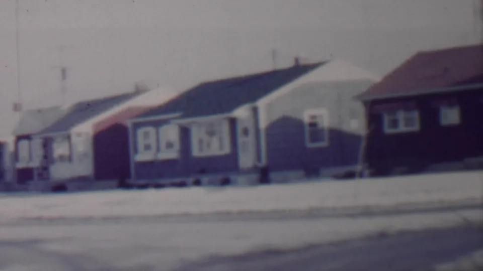 A 1962 8mm home-movie frame shows a snow-covered suburban street in Lincoln, Nebraska, with modest single-story bungalows and low front yards.
