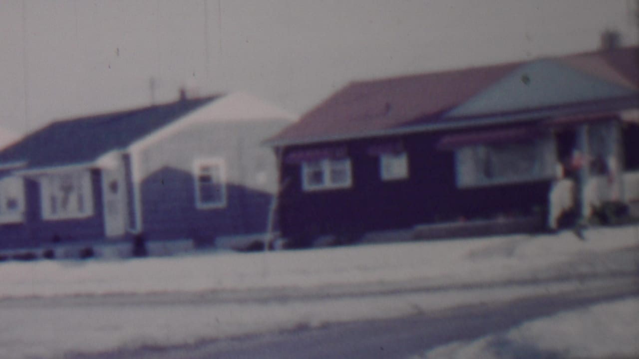 Bungalows on a snowy street with a person near a porch at right.