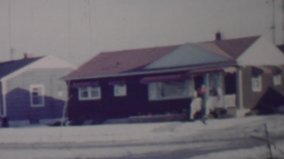 The frame shows a row of modest bungalows on a snow-covered Lincoln, Nebraska street, including a person in light clothing near the entrance of a darker house.