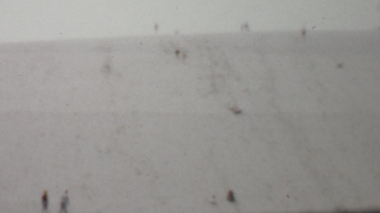 1959 United States 8mm home-movie frame showing small distant figures on a broad, faded hillside with soft focus and film specks.