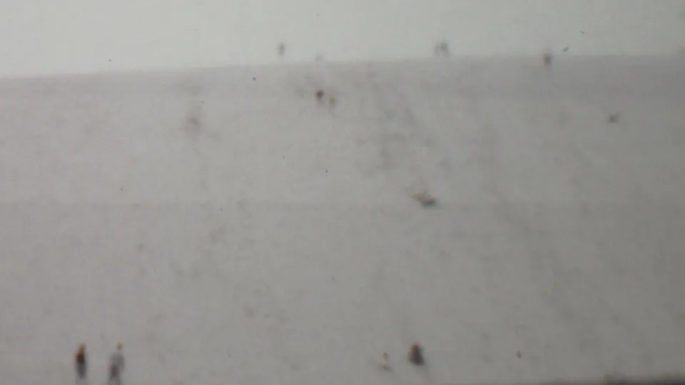 1959 United States 8mm home-movie frame showing small distant figures on a broad, faded hillside with soft focus and film specks.