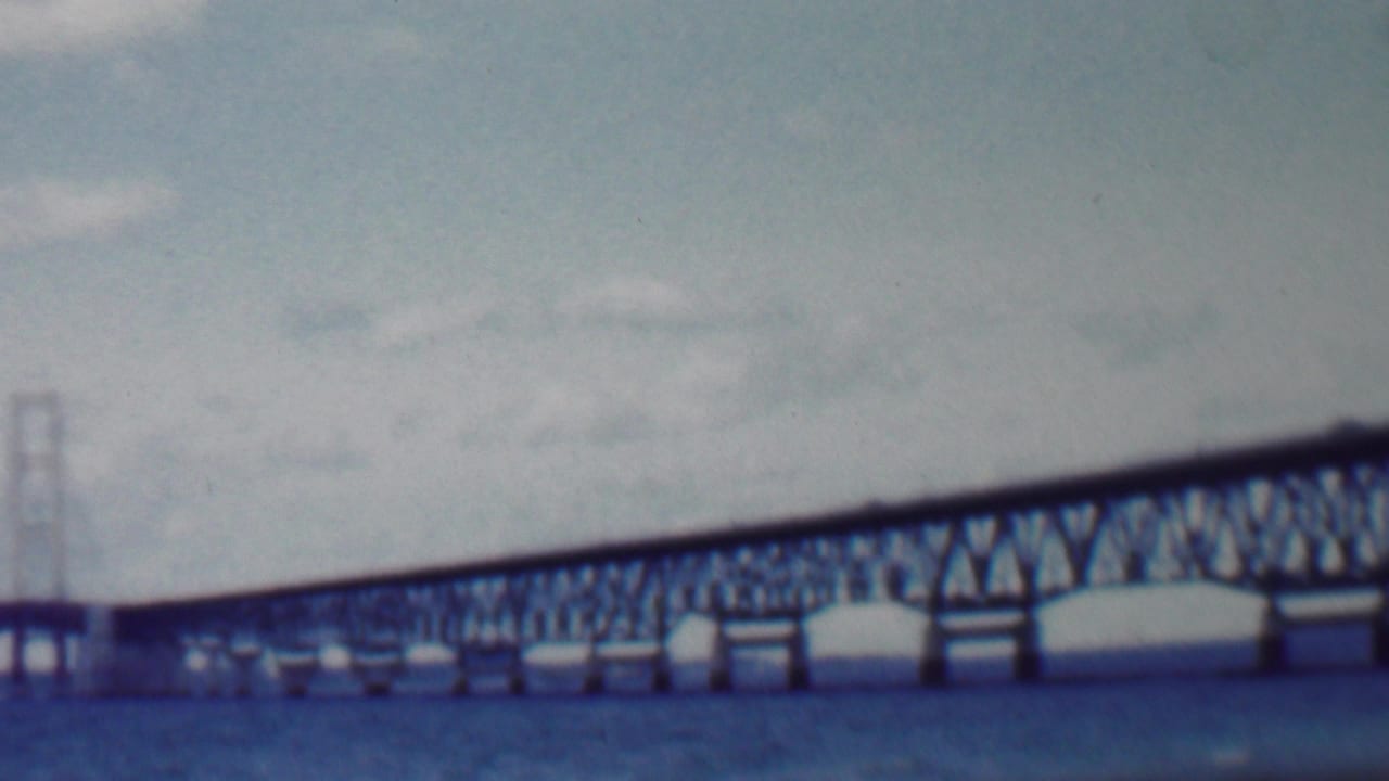 1959 Louisiana home-movie frame showing a long steel truss bridge over choppy water, with distant towers and a soft faded 8mm look.