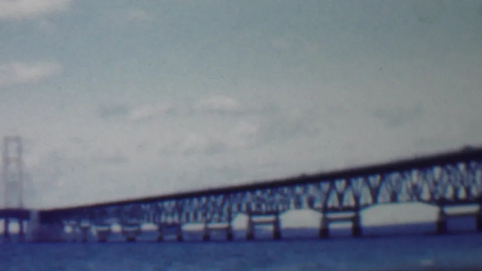 1959 Louisiana home-movie frame showing a long steel truss bridge over choppy water, with distant towers and a soft faded 8mm look.