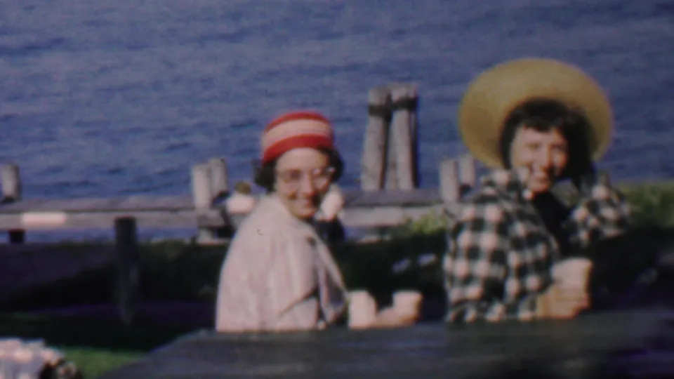 At the end of the clip, the two women are still seated at the waterfront table in the Louisiana home movie, with cups, hats, and the blue water behind them.