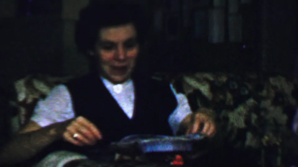 The woman sits in the dim private interior, smiling slightly as she handles a shallow box or tray associated with the gift.