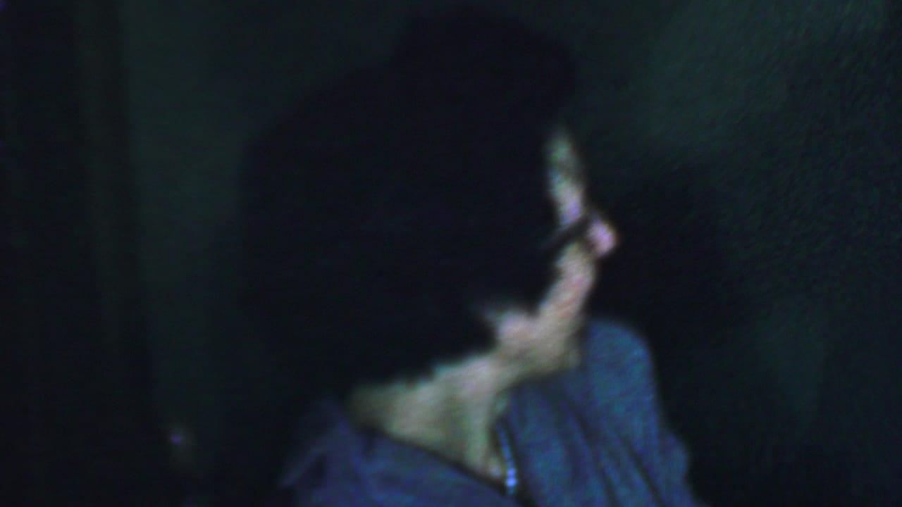 Woman wearing glasses looks away in a dim, grainy frame.