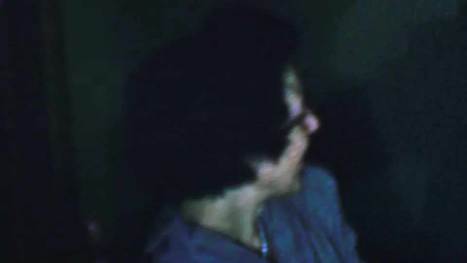 A woman in glasses looks away from the camera in a dark, soft-focus 8mm frame associated with the supplied 1959 Omaha metadata.